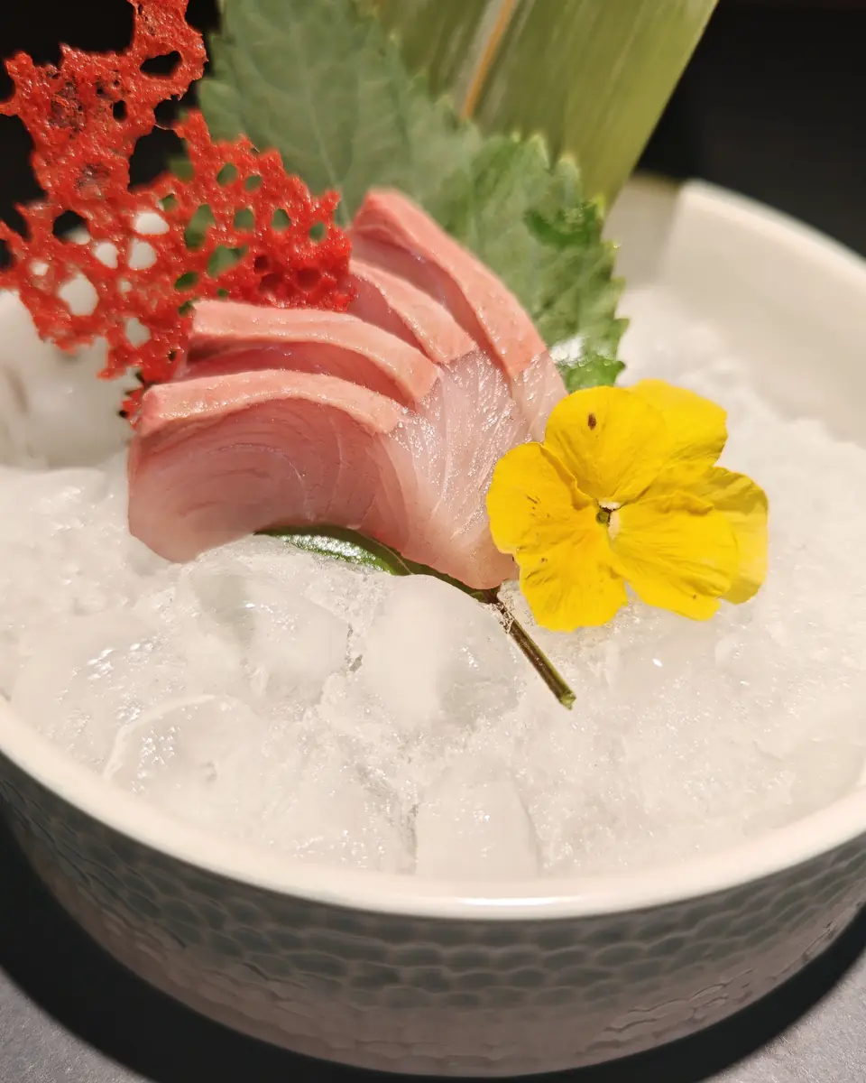 Sashimi su ghiaccio tritato con foglia di shiso, cialda rossa e una viola gialla