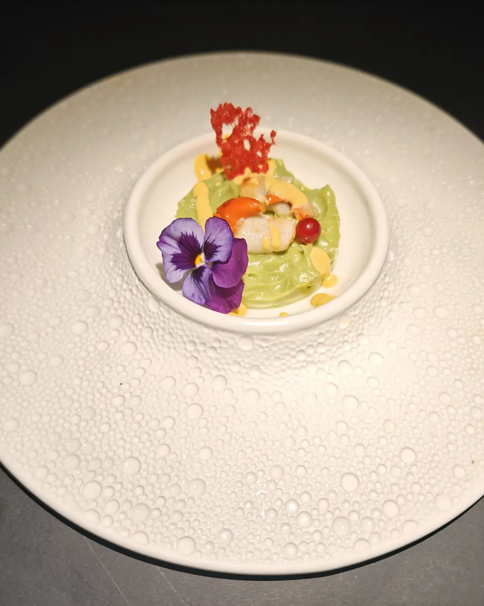 Mousse di avocado con frutti di mare e una viola, in una ciotolina su piatto bianco