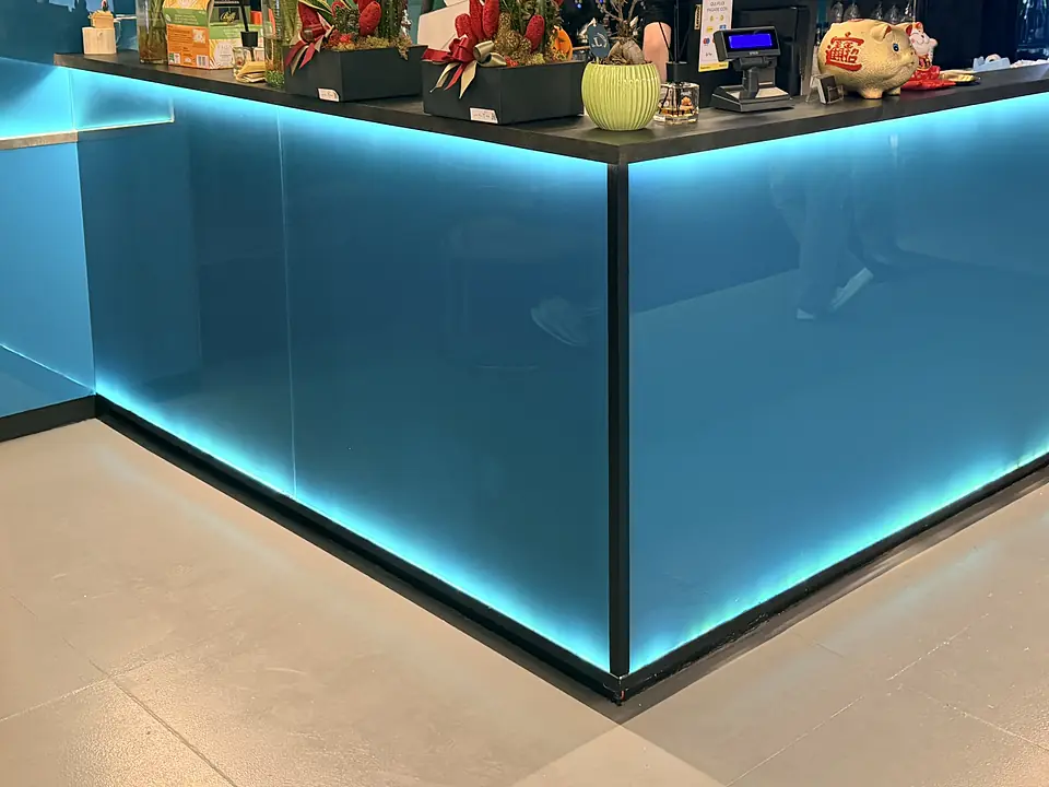 Il bancone del bar, rivestito di vetro azzurro illuminato dal basso, con piante e la cassa sul piano